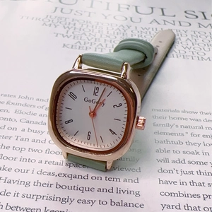 Vintage square quartz watch with green leather strap and gold case on a classic book page
