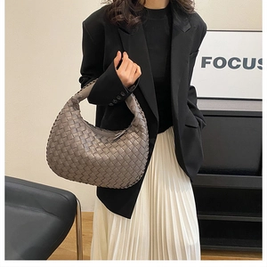 Fashionable taupe woven leather dumpling handbag for women held by a model in a blazer.