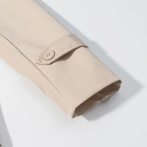 Dettaglio della manica del trench beige con cinturini ai polsi e un bottone rotondo su bianco