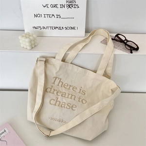 Detail of off-white canvas tote with brown embroidery and adjustable shoulder strap