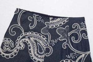 Close-up of white bohemian embroidery on dark blue denim waist with side zipper detail