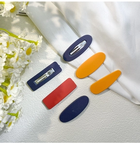 Detailed close-up of matte geometric hair clips in navy blue, yellow, and red colors