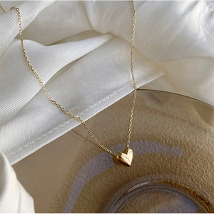 Macro shot of 18K gold plated silver heart pendant on white silk and amber glass background