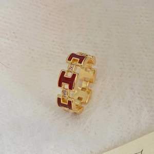 Macro shot of gold plated H letter ring with red enamel and zircon on plush background