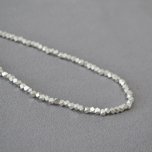 Macro detail of silver faceted metal beads on a minimalist textured fabric background