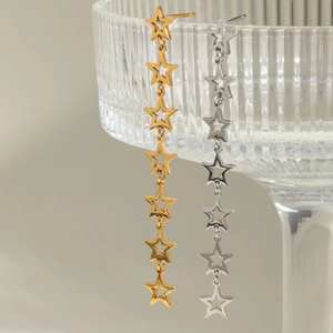 Elegant 18k gold and silver star tassel earrings hanging on glass with gray background
