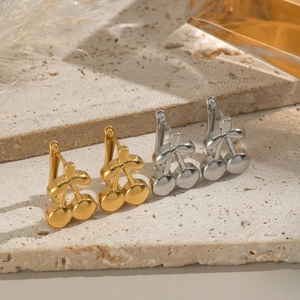 Polished 18K gold and silver cherry stud earrings displayed on a minimalist beige stone