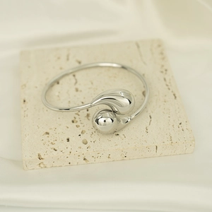 Detailed view of an asymmetric silver teardrop bangle on a textured travertine stone