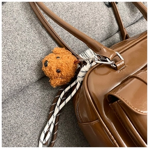 Close-up of brown glossy pillow bag with plush teddy dog charm and woven strap detail