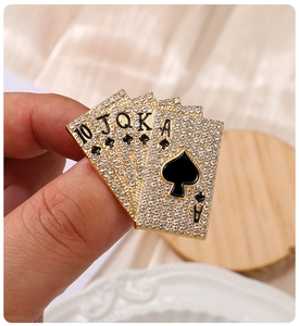 Détail d'une broche poker quinte flush en alliage doré avec strass blancs et émail noir