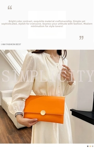 Elegante borsa a bustina arancione con catena dorata indossata su un abito a pieghe