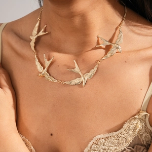 Detailaufnahme goldener Schwalben-Anhänger an einer minimalistischen Pulloverkette