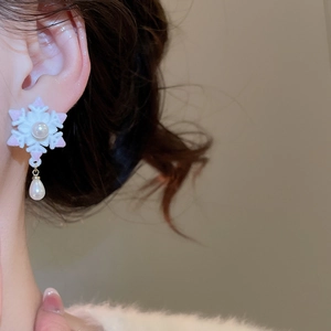 Détail d'une boucle d'oreille flocon de neige avec flocage blanc, accents dorés et perle