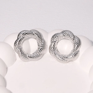 Silver flower stud earrings with hammered texture on a minimalist white ceramic tray
