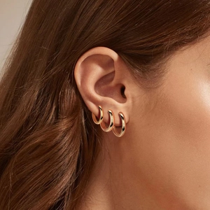 Detailed view of three polished gold hoop earrings layered on model's ear