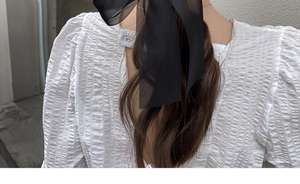 Close-up of a black mesh ribbon bow hair clip on a model wearing a white puff sleeve top