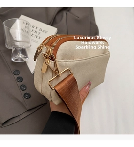 Close-up of double zipper detail on beige canvas crossbody bag with golden hardware