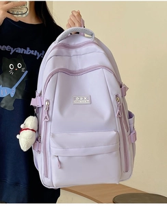 Detail of light purple nylon backpack featuring multi-pocket design and plush cat pendant