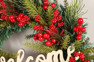 Close-up of artificial pine needles, red berries and welcome wood sign on Christmas wreath