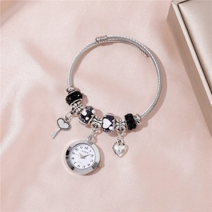 Detailed close-up of a silver beaded watch bracelet with heart and key charms on pink satin