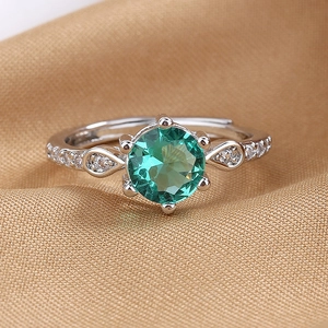 Silver six-prong ring featuring emerald green gemstone and pear-shaped accents on gold silk