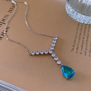 Silver teardrop necklace with blue gemstone and zircon V-shaped pendant on vintage background