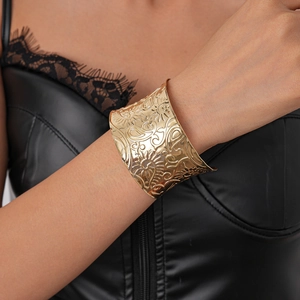 Detailed close-up of wide gold cuff bracelet featuring intricate paisley embossed patterns