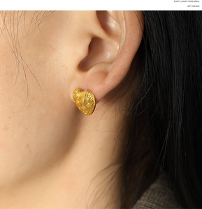 Close-up of a gold heart-shaped stud earring with a woven texture worn on a model