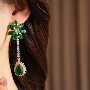 Macro shot of gold floral drop earrings with green zircon crystals on model