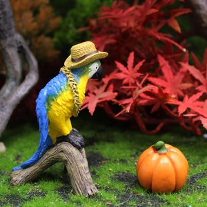 Resin parrot figurine with straw hat and mini pumpkin on autumn forest moss background