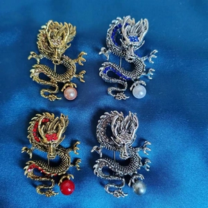 Detailaufnahme von vier Drachen-Broschen mit bunten Strasssteinen auf blauem Seidenstoff
