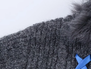 Detailed close-up of dark grey chunky knit fabric with fur pompom and blue ribbon accent