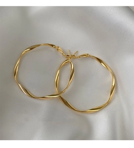 Macro shot of large gold twisted hoop earrings elegantly placed on white silk fabric