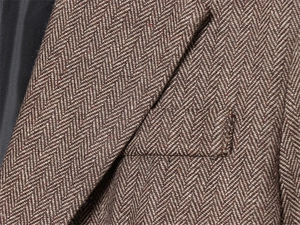Close-up of herringbone tweed texture and pocket stitching on a tan wool blazer