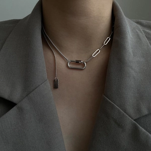 Gros plan d'un collier asymétrique argenté de style industriel porté sur un blazer