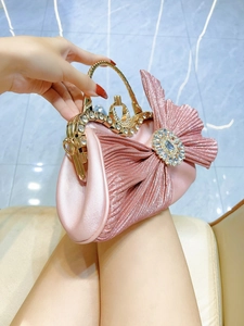 Pink pleated evening clutch bag with bow and rhinestones shown on model's hand