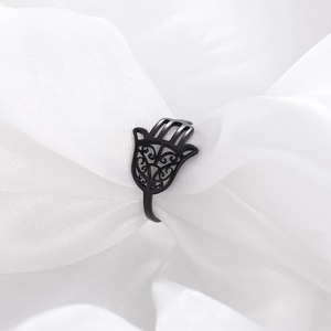 Close-up of black stainless steel Hamsa hand ring with hollow patterns on white fabric