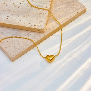 Minimalist gold heart pendant necklace with fine bead chain on beige stone background