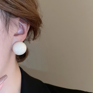 Close-up of a large glossy white spherical stud earring worn on a model's ear