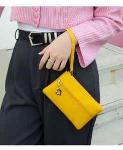Close-up of bright yellow wristlet bag with gold heart charm and zipper detail
