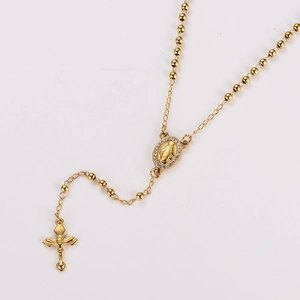 Macro detail of gold beaded necklace with Virgin Mary oval pendant and small cross charm