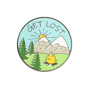 Detail of round enamel pin showing mountain landscape with campfire and GET LOST text