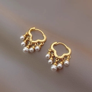 Elegant gold hoop earrings with five white pearl pendants on soft beige fabric background