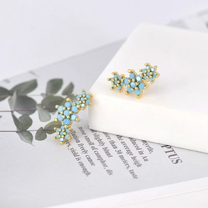 Macro detail of golden wing-shaped earrings featuring vibrant turquoise blue zircons