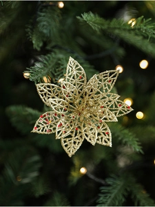 Détail d'une fleur de poinsettia dorée ajourée avec paillettes sur un sapin