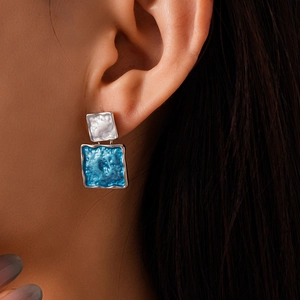 Detail of geometric blue and silver square drop earrings with hammered metal texture