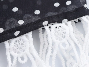 Close-up of black polka dot fabric featuring delicate white lace tassel trim detail