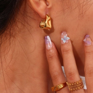 Close-up of golden irregular geometric earrings and textured rings on a model