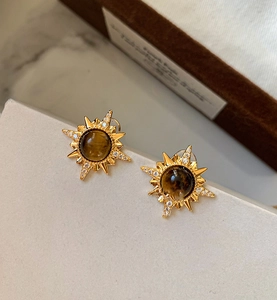 Détail macro de boucles d'oreilles en étoile plaqué or 18K avec incrustation d'oeil de tigre