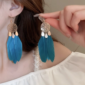 Detail of bohemian drop earrings featuring peacock blue feathers and gold hollow metal disks
